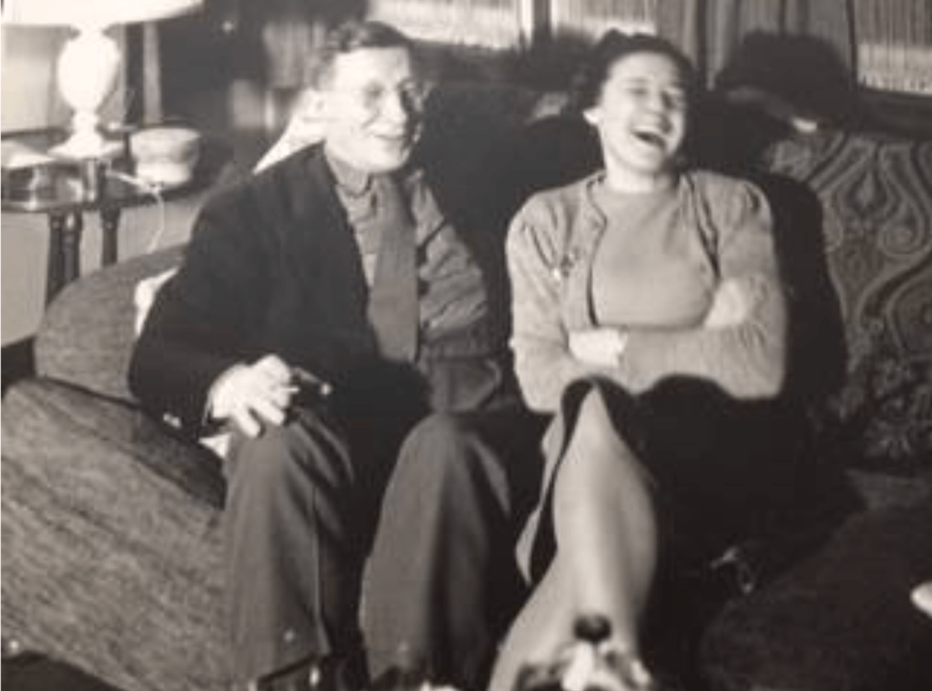 Sir Fred and Lady Banting sat on a sofa, Fred to the left and Henrietta on the right. Both laughing.